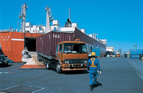 写真：運搬船からコンテナがトラックに積まれて運び出される様子